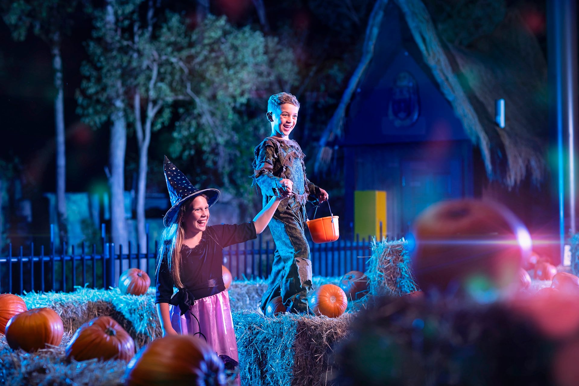 Two children dressed in Halloween costumes trick-or-treating among pumpkins and hay bales at Dreamworld’s Happy Halloween event.